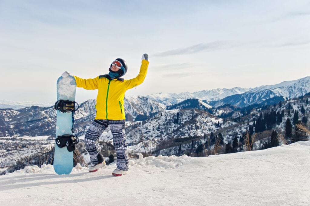 Young woman snowboarder in a yellow jacket and black helmet on the background of snowy mountains